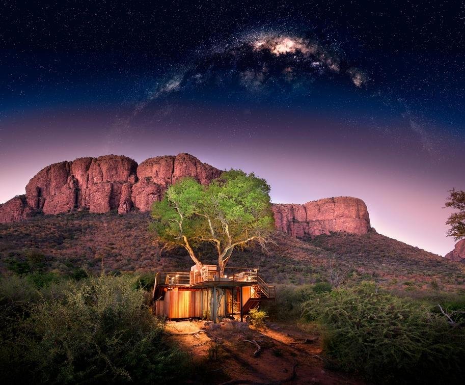 Lit treehouse beneath red cliffs and the Milky Way on a tailor-made safari